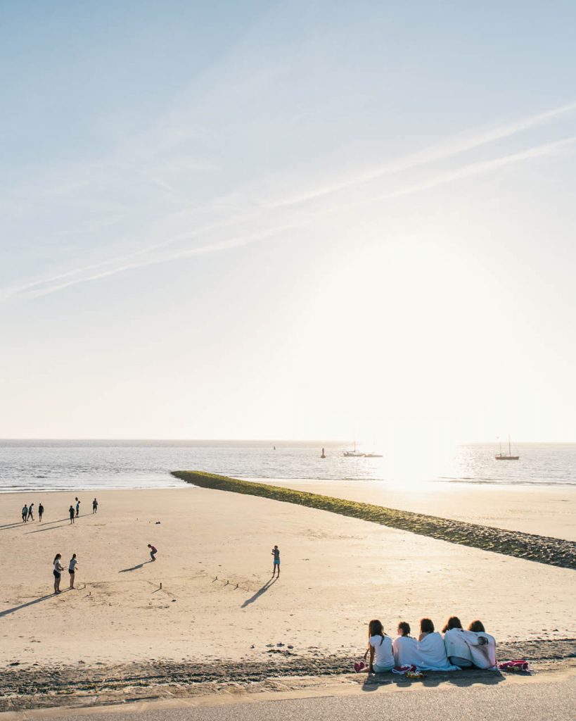 Kinder im Urlaub auf Norderney sitzen am Strand und blicken aufs Meer